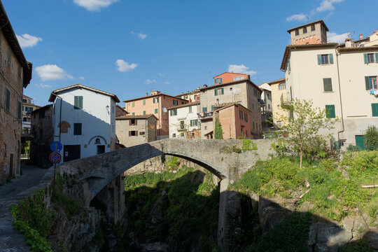 View of the historic Romanesque bridge spanning a deep gorge surrounded by traditional stone houses and lush greenery in Loro Ciuffenna, Tuscany, Italy.