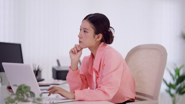 Asian businesswoman thinking using laptop computer working at desk in modern office thoughtful focused professional woman browsing internet researching online