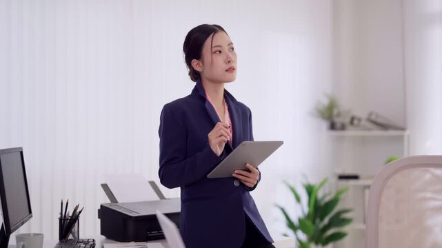 young Asian businesswoman professional wearing formal suit holding tablet device with stylus pen concentrate review document check business report data