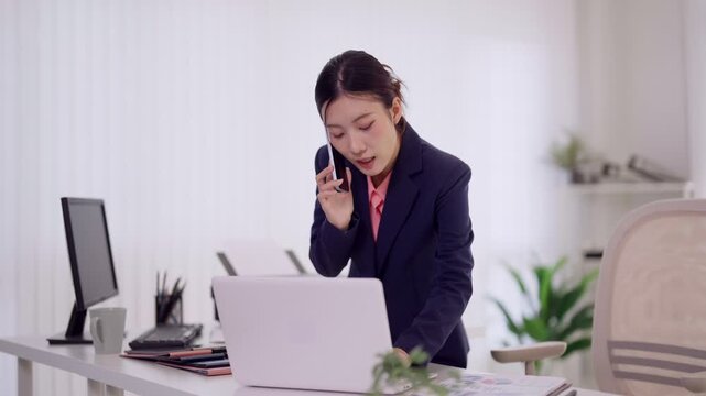Asian businesswoman professional phone call multitask review document working standing modern office desk laptop computer communication corporate executive