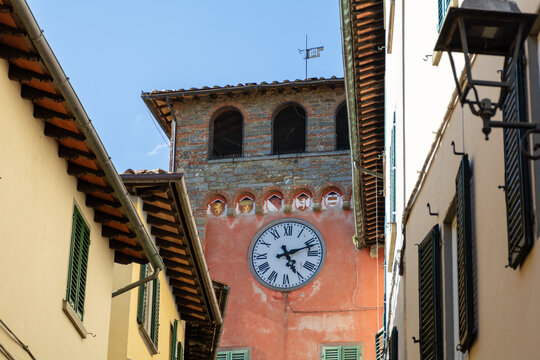 View of the historic clock tower and traditional buildings along a narrow street in Loro Ciuffenna, Tuscany, Italy.