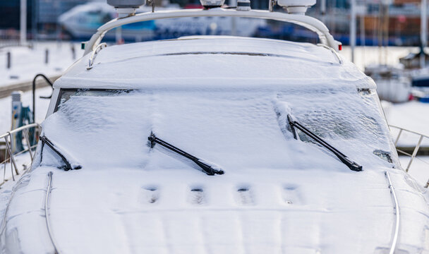Front view of snow covered yacht with icy windshield in harbor.