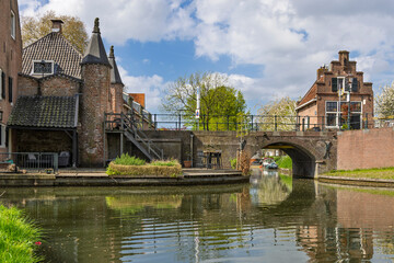 Fototapeta premium Ijsselstein, Netherlands. A picturesque view of an ancient brick building and a small arched stone bridge reflected in the calm waters of a town canal.