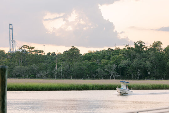 Small motorboat cruising through a calm marsh waterway in at dusk