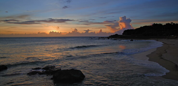 Golden sunset over a sandy beach with gentle waves and dark shoreline