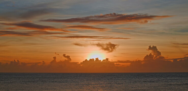 Golden sun rising over the calm ocean horizon with soft orange clouds