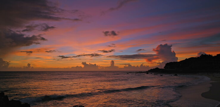 Vibrant sunset sky over rocky coastline with utility poles at dusk