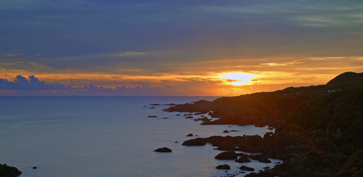 Sunset sky with vibrant orange and purple clouds above a dark ocean