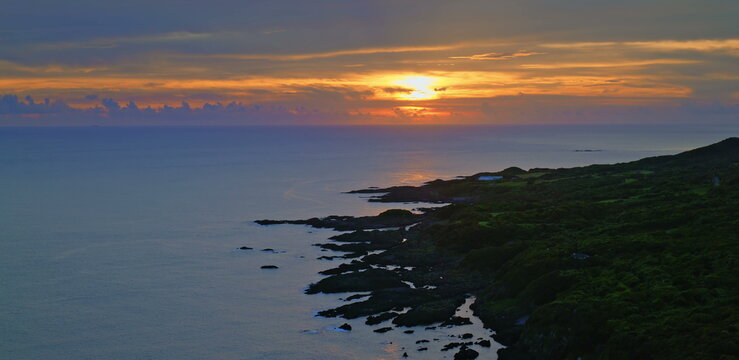 Sunset sky with vibrant orange and purple clouds above a dark ocean