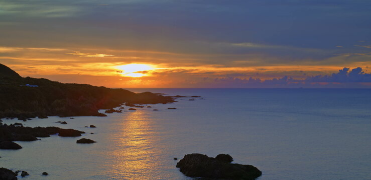 Sunset sky with vibrant orange and purple clouds above a dark ocean