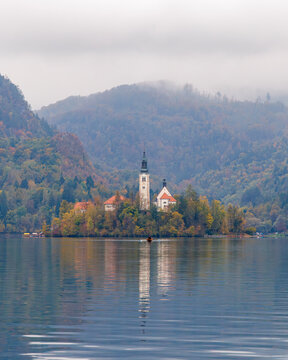 View of the Pilgrimage Church of the Assumption of Mary on Bled Island surrounded by autumn foliage and misty hills reflected in the calm lake water Bled, Radovljica, Slovenia.