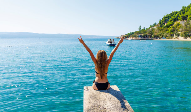 woman in bikini with arms raised facing the sea summer vacation and freedom concept