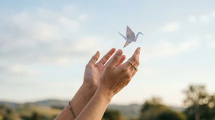 Fototapete Kraniche Hands releasing a white paper origami crane into the sky for peace  © RAAL