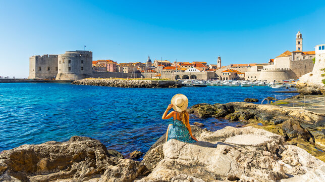 woman with straw hat and bleu dress looking at dubrovnik old town and fort st john in croatia
