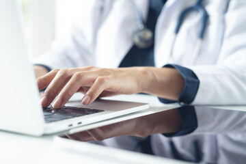 Fototapeta premium Female doctor hands typing on laptop computer in medical office, close up