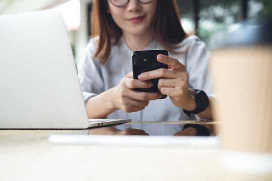 Asian woman using smartphone while working on laptop computer with digital tablet on table at outdoor cafe, surfing the net, remote work, online business 