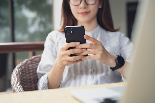 Young asian woman using smartphone with laptop on table, remotely working at outdoor cafe or modern workspace, digital nomad lifestyle, freelance at work