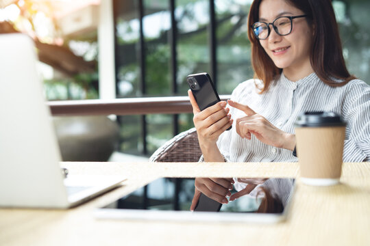 Smiling asian woman using smartphone during remote working with laptop and tablet on table at outdoor cafe. 