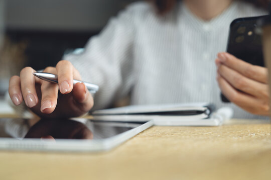 Woman using digital tablet and smartphone with note book on table, planning business meeting agenda, working at office. close up