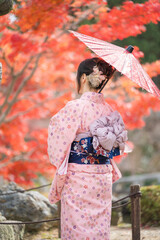 Rear view of a woman in a floral yukata holding a red paper umbrella against colorful autumn foliage background. Kyoto, Japan. © Shawn.ccf