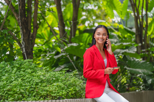 Young Asian Woman talking on a smartphone while holding a credit card in a garden