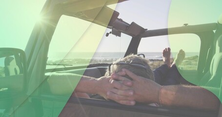 Reclining man propping bare feet on dashboard in open SUV at beach, wearing sunglasses and bracelet © vectorfusionart
