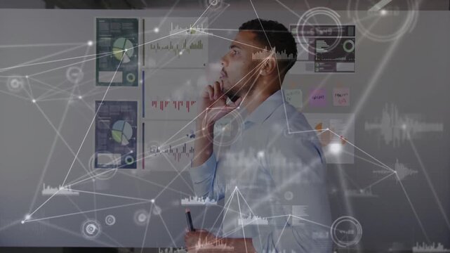 Male analyst scanning wall charts, tapping phone in office activating HUD linking graphs for design