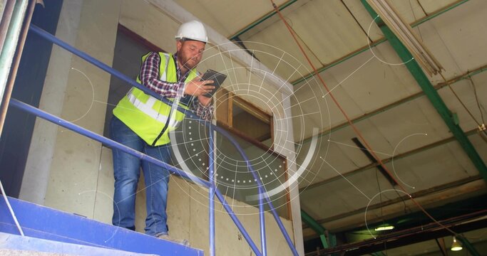 Leaning site worker checking tablet on platform at warehouse, white hardhat, neon vest, copy space