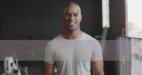 Smiling mid-adult man wearing gray tshirt facing lens in gym with rower railing window and scanline © vectorfusionart
