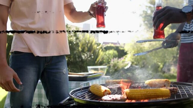 Static clearing, two men cooking at kettle grill, flipping corn and patties, toasting for barbecue