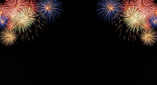Vibrant fireworks explode in blue red and yellow against a dark night sky