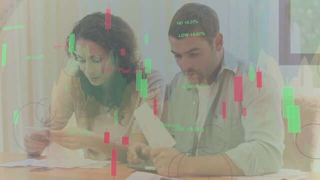 Couple reading bills, using calc, sorting receipts while candlestick charts overlay for budgeting