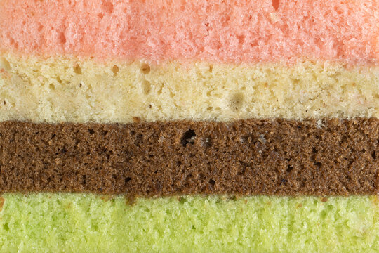 Close-up macro texture of layered sponge cake with four distinct colors: pink, vanilla, chocolate, and green.