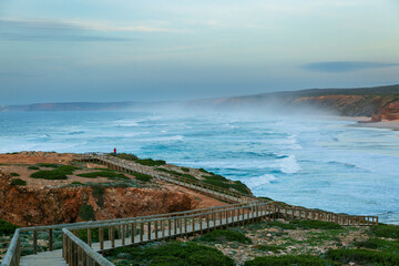 Obraz premium Lone Tourist on Coastal Boardwalk Above Rough Ocean in Algarve