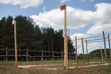 Fototapeta premium Checkpoint number 2 on a wooden pole with a red flag. Training course markings on the ground. Tall pine forest in the background