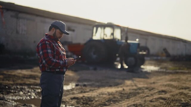 Traditional agriculture and modern agribusiness, farmer controlling tractor work . Farm owner using modern smartphone with mobile app for agronomist, farmland and agronomy, agricultural machinery