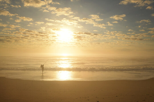 Teen girl casting fishing pole on beach at sunrise Outer Banks N