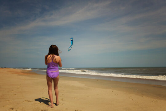 Behind young girl flying kite on beach blue sky Cape Hatteras Na