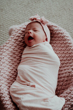 Newborn baby girl swaddled laying on pink blanket