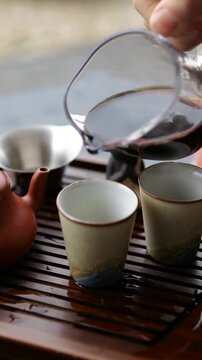 Pouring dark pu erh tea from a glass fairness pitcher into a ceramic cup during a traditional chinese gongfu tea ceremony, with a buddha statue in the background for a mindful experience