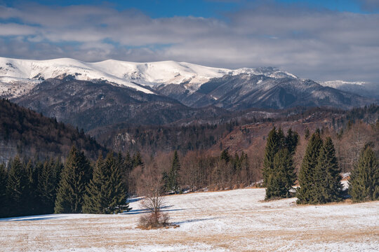 View of Hruby vrch with snow-capped mountain peaks and evergreen forests above a frost-covered meadow Balaze, Banska Bystrica Region, Slovakia.