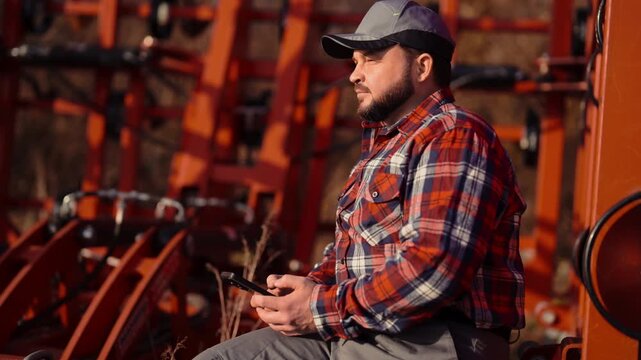 Male farm worker resting and surfing internet by smartphone, phone addiction. Villager works in ranch, rural lifestyle in countryside, farmer testing mobile app for agribusiness and finance control