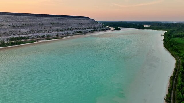 Aerial video of turquoise waters of Auvere ash pond near Narva, Estonia, with rippled surface, quarry landscape, and greenery at sunset. Drone slowly moving forward