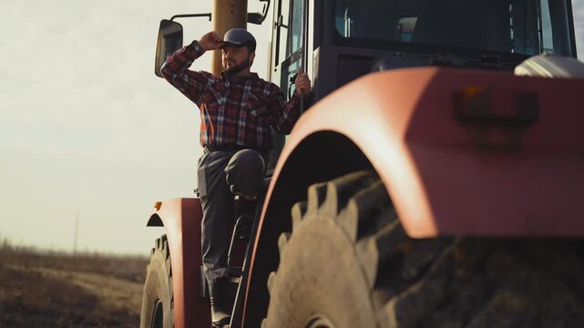 Professional tractor driver posing on huge agricultural machinery for harvesting . Successful farmer looking around his own farmland, planning sowing, epic portrait of villager in rural landscape