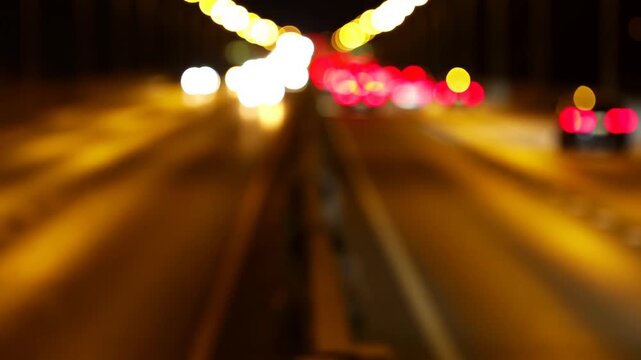 Slow motion tracking handheld pan of cars with blurred lights streaking along urban highway bridge at night with golden bokeh glow and passing traffic