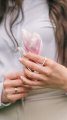Naklejka premium Woman holding a delicate pink magnolia flower with pearl ring and wedding band