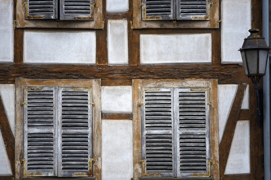Antique half-timbered house facade with wooden window shutters and a vintage brass lantern in Molsheim Alsace, France.
