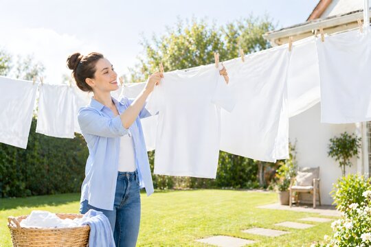 Frau h&auml;ngt frische weisse W&auml;sche im Garten an die Leine bei Sonnenschein