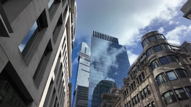 London's financial district skyline featuring modern glass skyscrapers reflecting the blue sky and clouds, surrounded by historic architecture and business office buildings