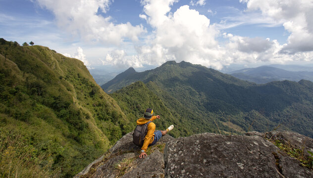 Solo traveler sitting on a cliff overlooking lush green mountains in Thailand. Peaceful introvert lifestyle, freedom, self reflection and quiet escape in nature landscape